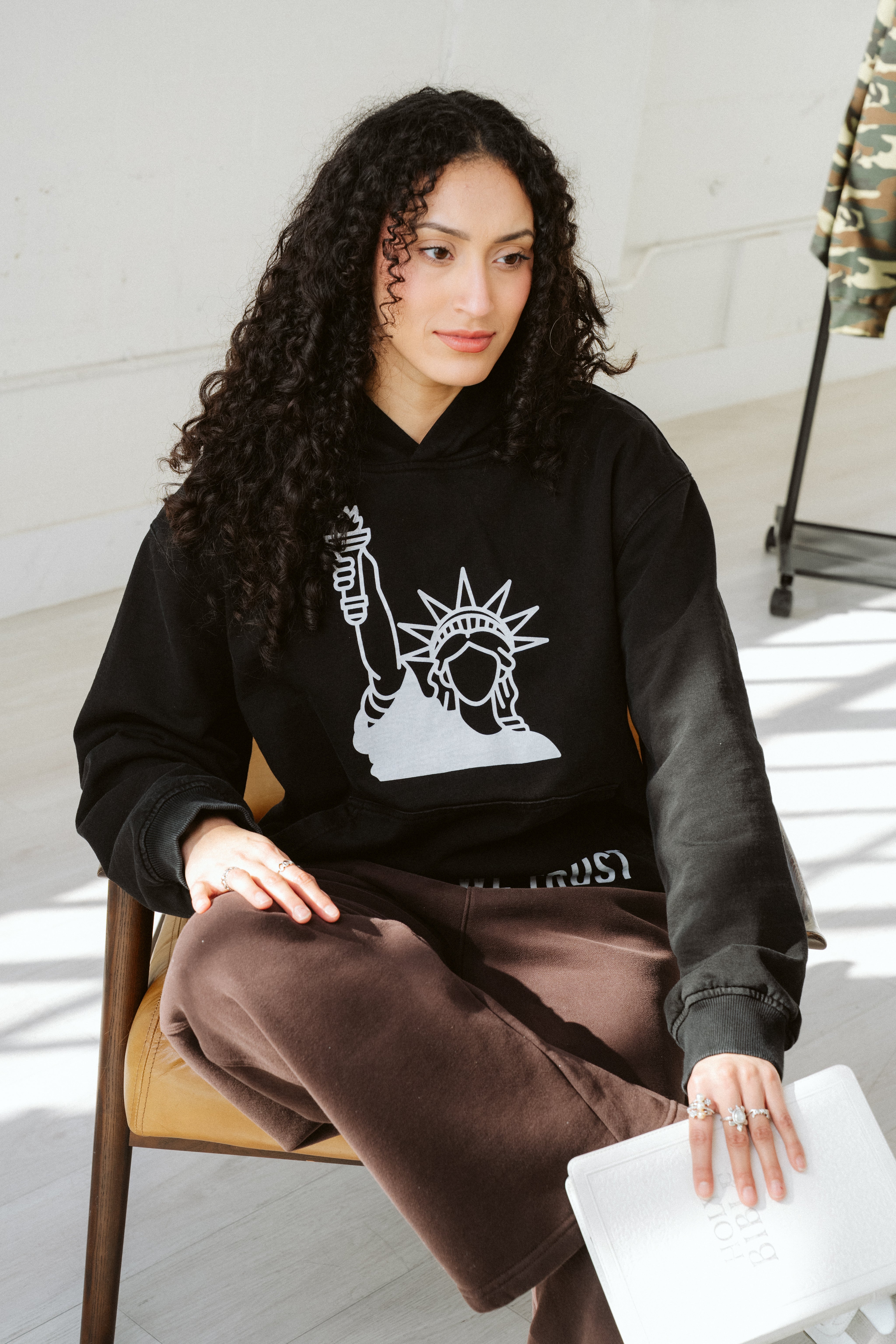 Woman wearing a black hoodie with a white graphic design, sitting on a chair indoors.